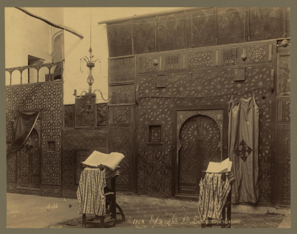A Coptic church interior: an inlaid wooden screen with an arched door, and two lecterns before it, each holding an open book