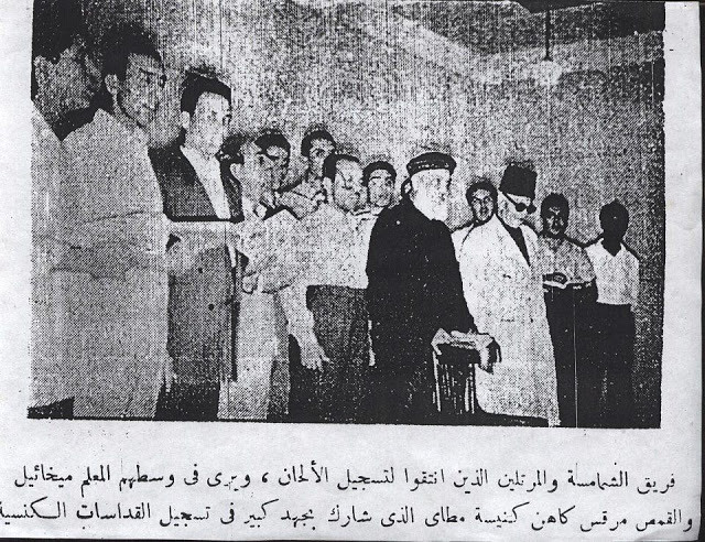 A newspaper photograph of a crowd of men in a room, a bearded priest in a black cap and a blind man in dark glasses and a tarbush at its centre, with an Arabic caption beneath