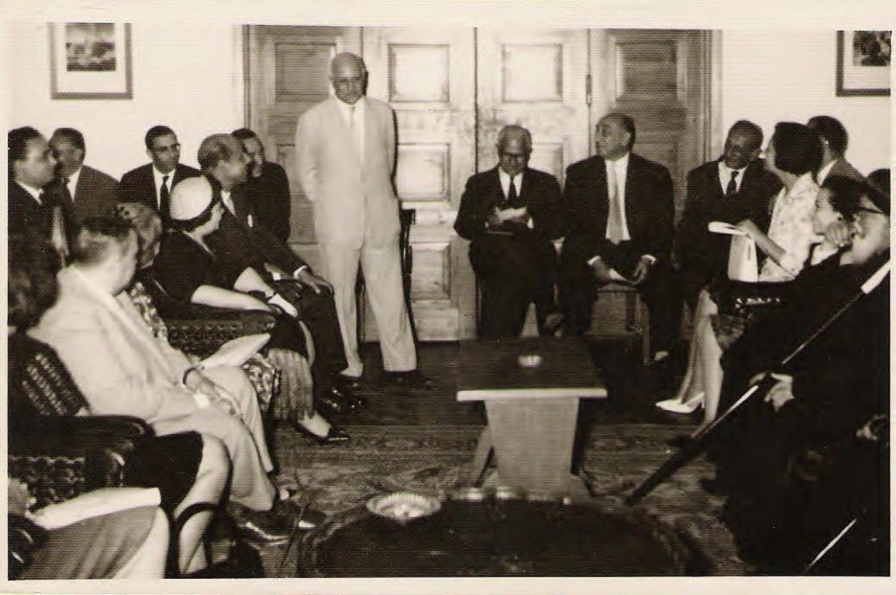 A man standing in a salon speaks to a seated audience of men and women