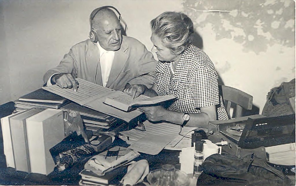Ragheb Moftah, wearing headphones, and Margit Tóth study a handwritten score at a table piled with volumes