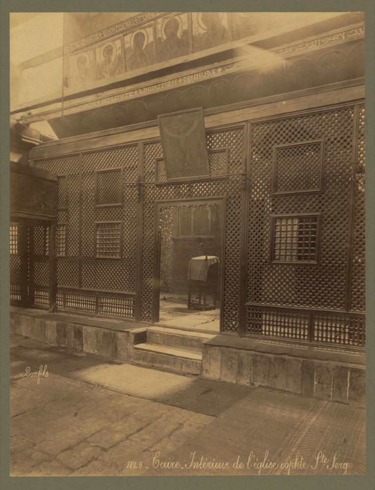 The dim interior of an old Coptic church: a tall screen of wooden latticework with icons along its top